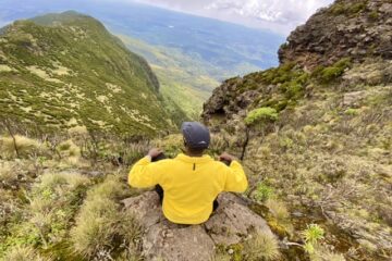 Hiker in a yellow fleece jacket sitting on a cliff - high altitude hiking
